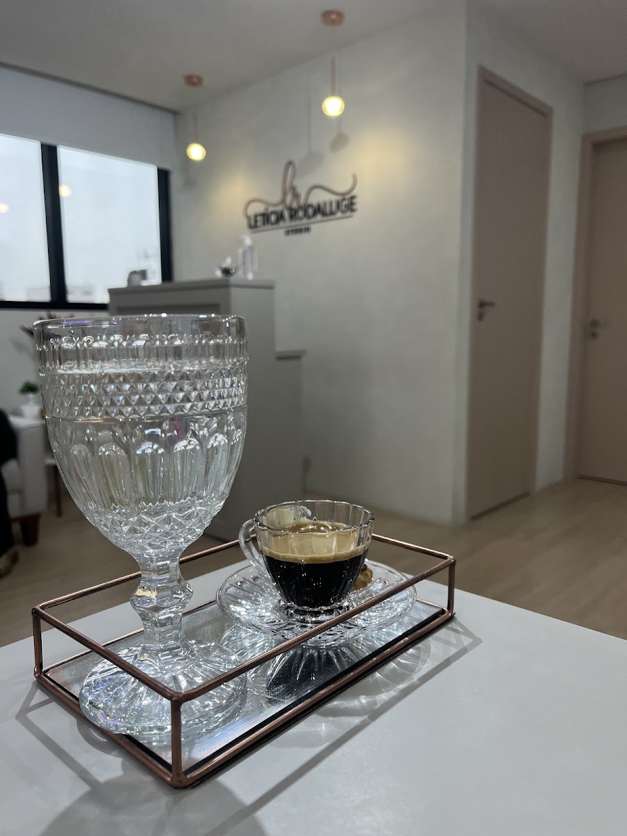 Bandeja com café e água em taça de cristal, com o logo do estúdio ao fundo